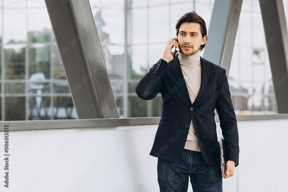 Portrait of handsome modern male businessman in suit holding folder with documents and talking on the phone against the background of urban buildings and offices. Portrait of handsome modern male businessman in suit holding folder with documents and talking on the phone against the background of urban buildings and offices.