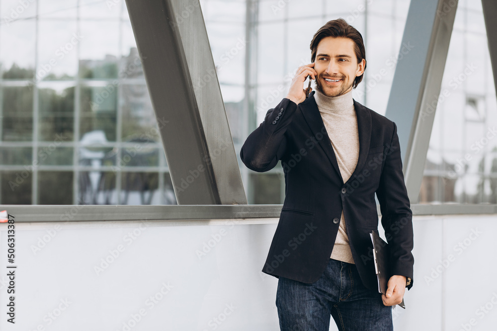 Portrait of handsome modern male businessman in suit holding folder with documents and talking on the phone against the background of urban buildings and offices. Portrait of handsome modern male businessman in suit holding folder with documents and talking on the phone against the background of urban buildings and offices.