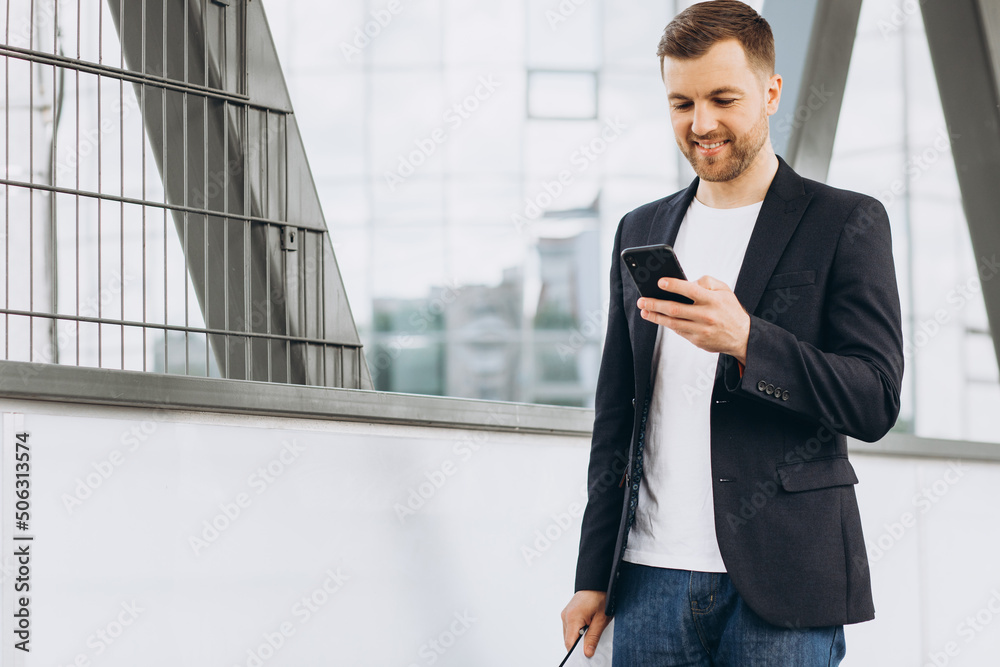 Portrait of handsome modern male businessman in suit walking smiling and reading or writing message on phone on background of urban buildings and offices. Portrait of handsome modern male businessman in suit walking smiling and reading or writing message on phone on background of urban buildings and offices.