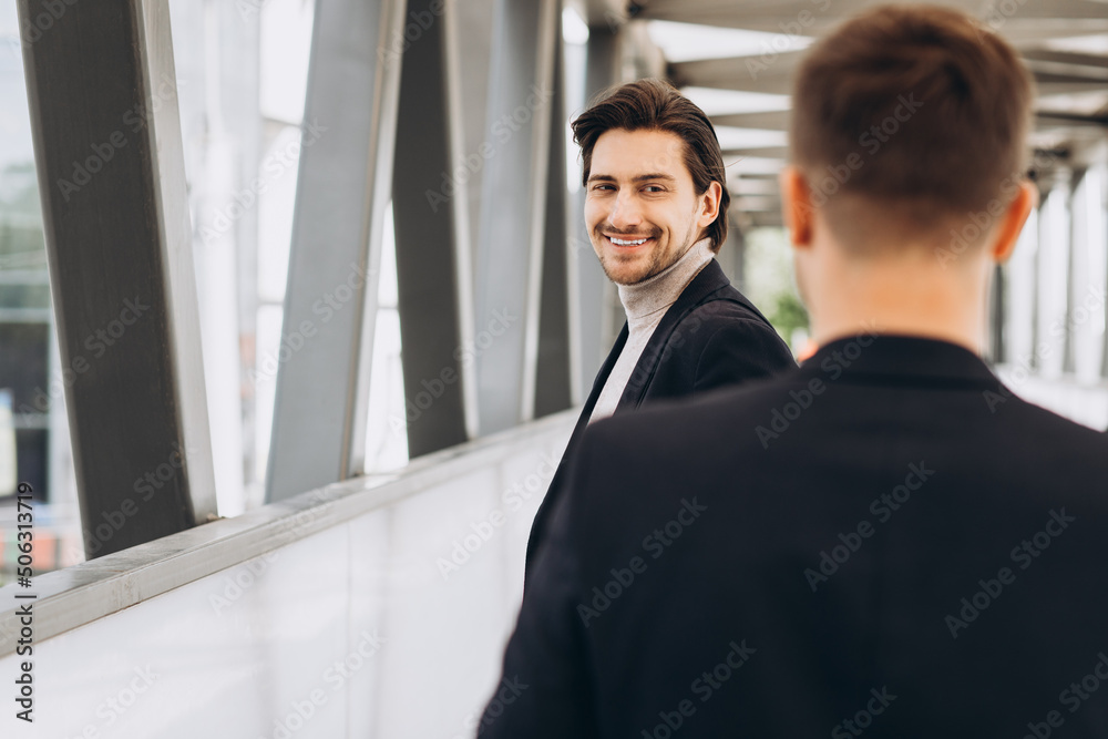 Two modern businesspeople greet each other smiling and saying something against the background of urban offices and buildings Two modern businesspeople greet each other smiling and saying something against the background of urban offices and buildings