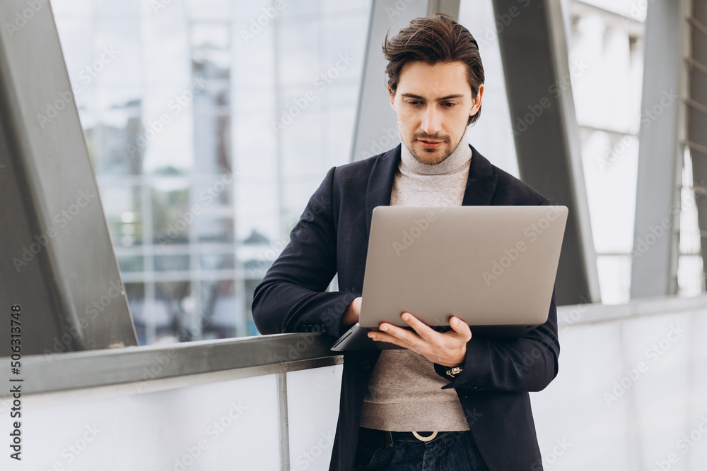 Portrait of handsome happy businessman man in suit holding laptop on background of urban buildings and offices. Portrait of handsome happy businessman man in suit holding laptop on background of urban buildings and offices.