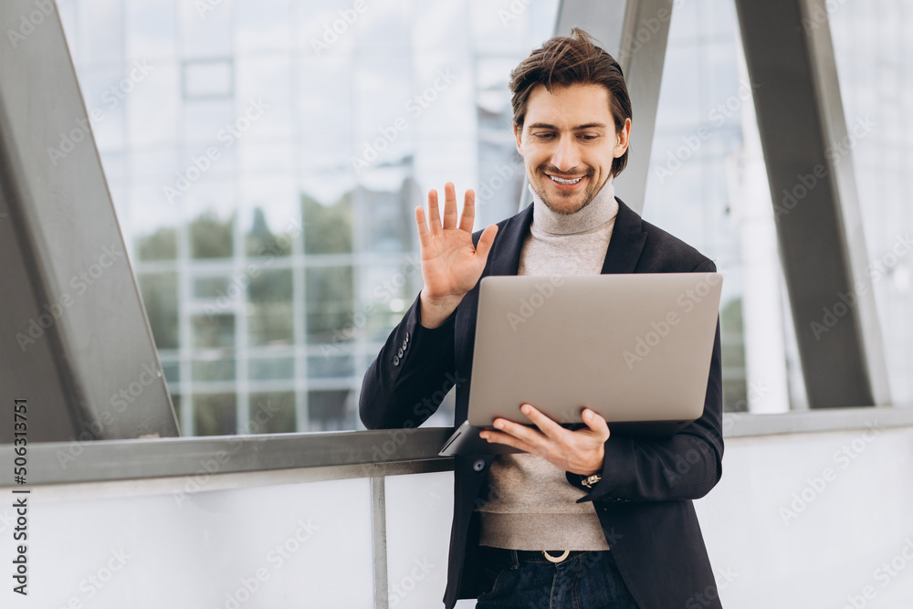 Portrait of handsome happy male businessman in suit holding laptop and having video call on background of urban buildings and offices. Portrait of handsome happy male businessman in suit holding laptop and having video call on background of urban buildings and offices.