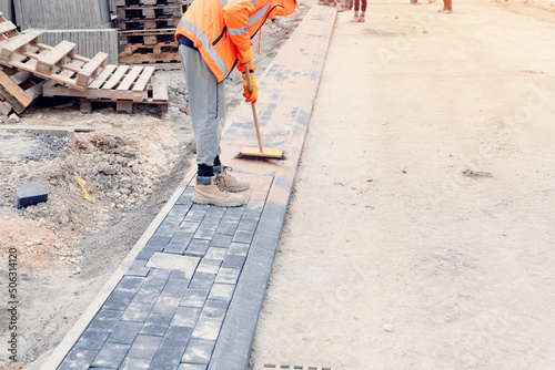 Paving stone workers filling joints of the block paved footpath with dry sand during the construction of a new road photo