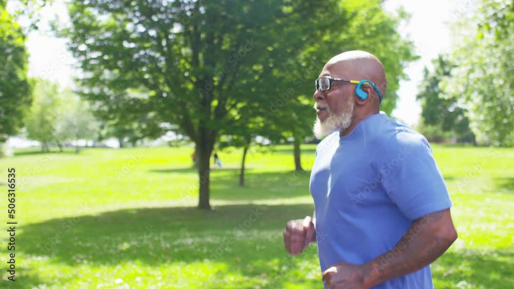 Handsome, senior male jogging through the park listening to music during the daytime, in slow motion