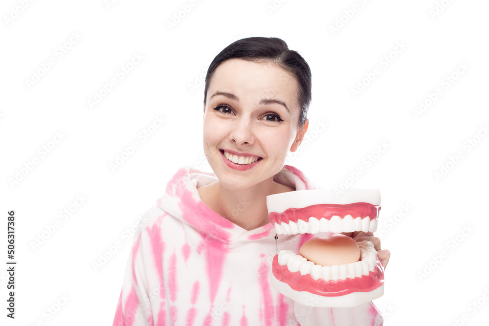 smiling woman in a pink hoodie holds a dental jaw in her hand, white background smiling woman in a pink hoodie holds a dental jaw in her hand, white background