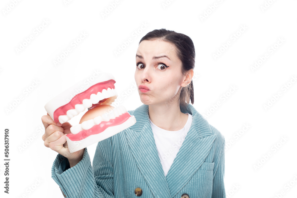 surprised woman in a corduroy jacket holds a huge jaw with teeth in her hand, white studio background surprised woman in a corduroy jacket holds a huge jaw with teeth in her hand, white studio background