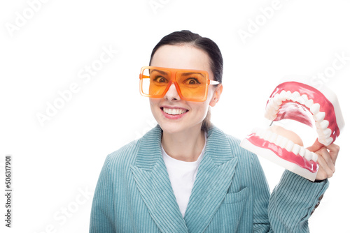 joyful woman in orange glasses, velvet jacket holds a huge jaw with teeth in her hand, white background