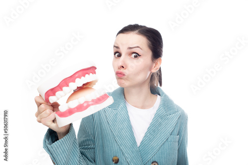 surprised woman in a corduroy jacket holds a huge jaw with teeth in her hand, white studio background