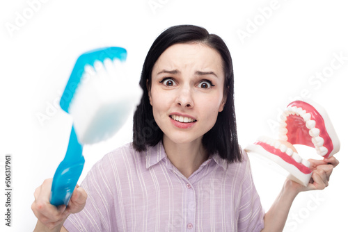 surprised woman in a purple shirt holding a huge toothbrush in her hand a huge jaw mockup