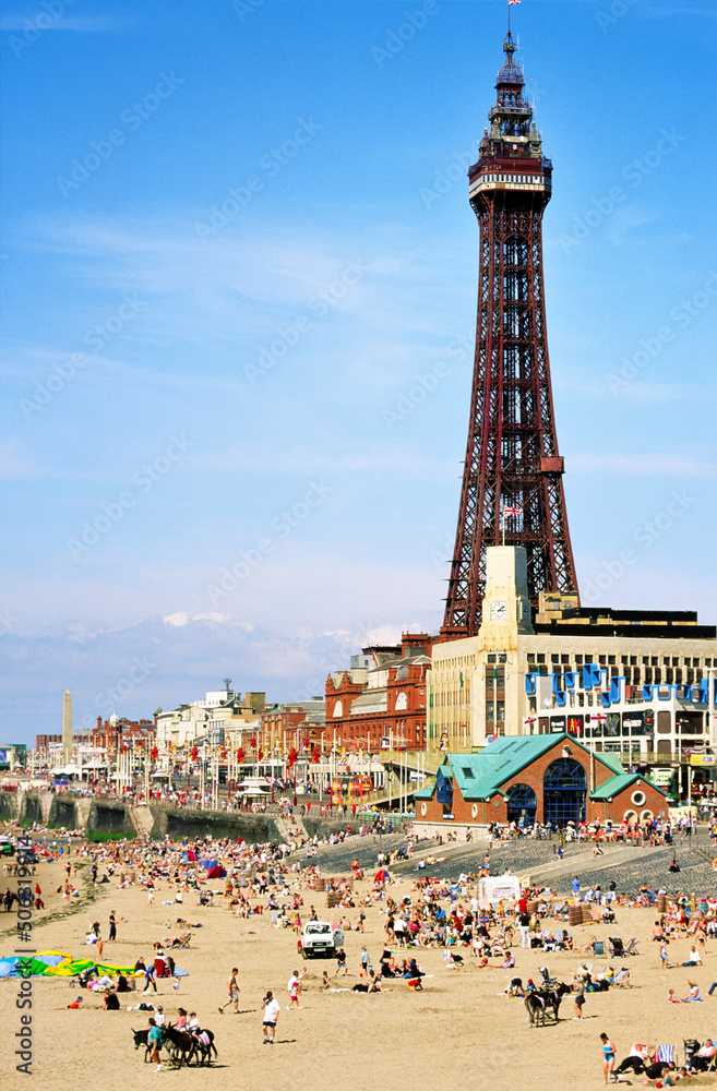English seaside summer holiday. People sunbathing on Blackpool Beach beneath Blackpool Tower, Lancashire, England.
