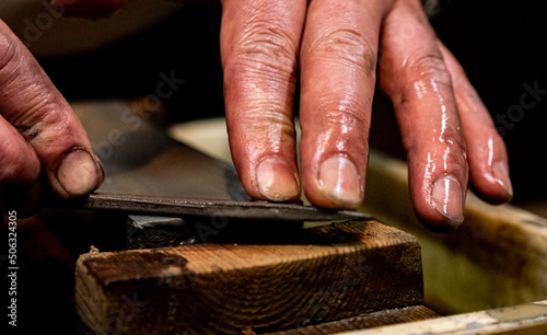 Obraz na plátně Master swordsmith is sharpening knife on grindstone with water