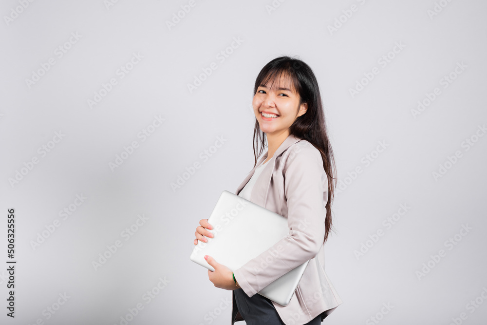 Side view woman smiling confident smiling holding closed laptop, Portrait excited happy Asian young female person hugging close cover computer device studio shot isolated on white background