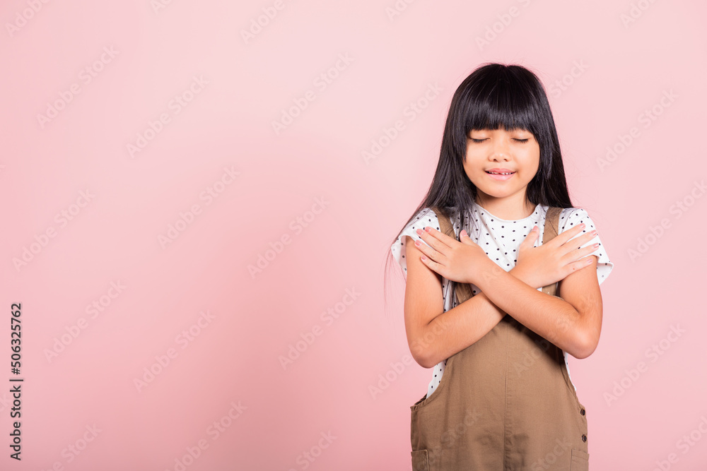 Asian little kid 10 years old doing grateful gesture and closed eyes at studio shot isolated on pink background, Happy child girl smile putting crossed palm on her chest, being thankful, Gratitude day Asian little kid 10 years old doing grateful gesture and closed eyes at studio shot isolated on pink background, Happy child girl smile putting crossed palm on her chest, being thankful, Gratitude day