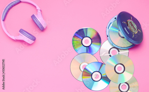 Personal compact portable CD player disks purple headphones on a pink background.