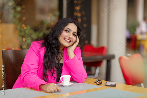 Portrait of a young and stylish Indian woman sitting in a cafe and enjoying a drink on the weekend