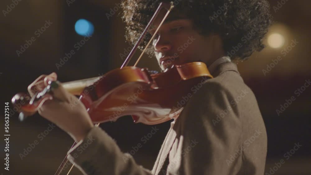 Low angle selective focus shot of young African American violinist playing fiddle during classical music concert