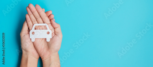 Hand holding paper Car cutout on blue background. Vehicle insurance, warranty, Automobile rental, Transportation, Maintenance and repair concept