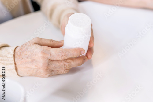 Close up hands of a senior woman holding a medical bottle and asking for information from the nurse before administering medication. Caregiver visit at home. Home health care and nursing home concept.