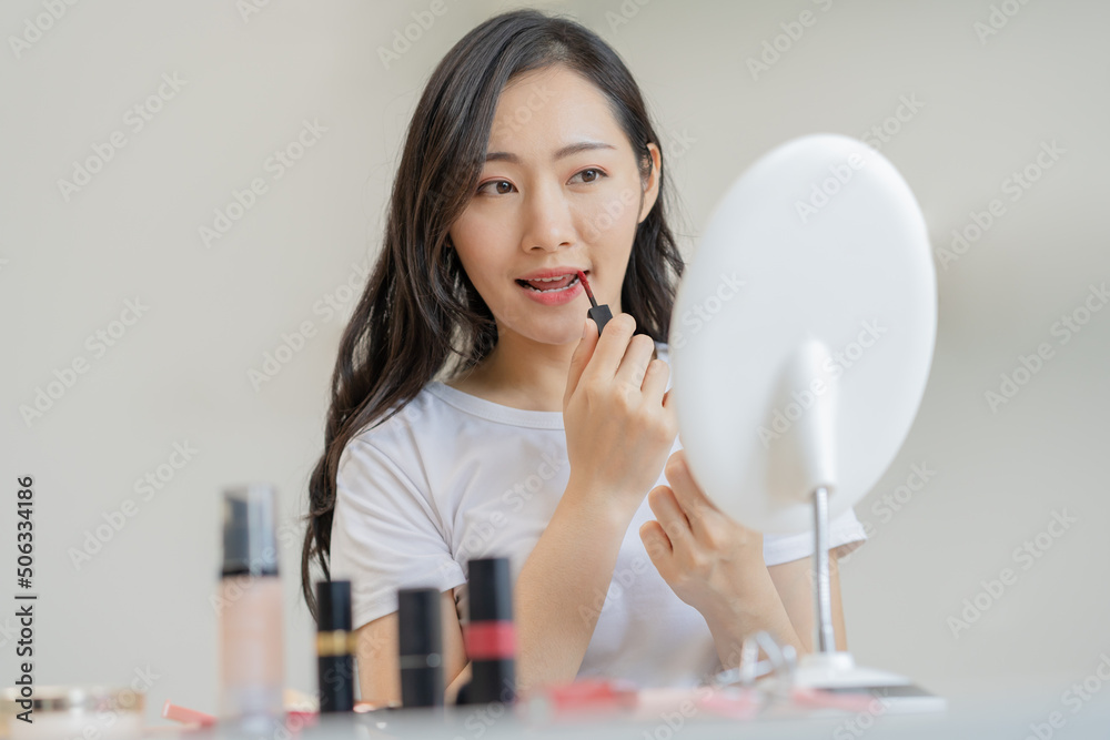 Beauty cosmetics concept, hand of asian young woman, girl make up face by applying lipstick, lips balm on her mouth, looking at the mirror at home. Female look with natural fashion style, skin care. Beauty cosmetics concept, hand of asian young woman, girl make up face by applying lipstick, lips balm on her mouth, looking at the mirror at home. Female look with natural fashion style, skin care.