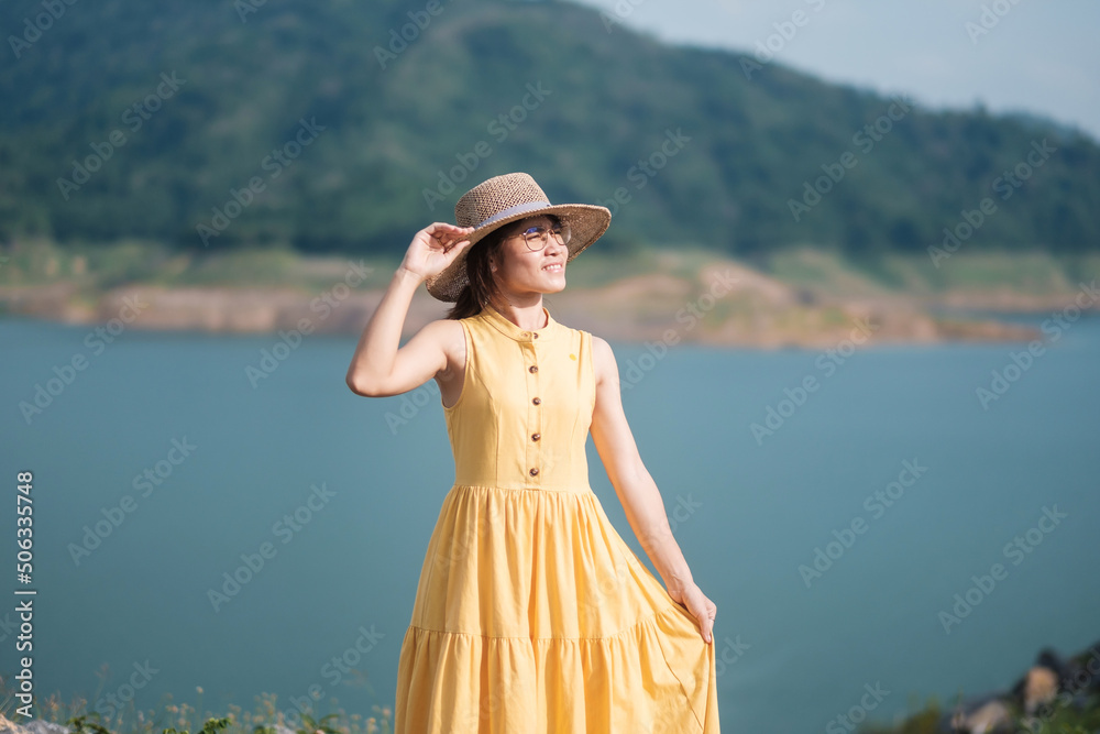 Asian Woman in yellow dress and hat Traveling at outdoor, Happy traveler looking to Khun dan Prakarnchon dam. landmark and popular for tourists attractions in Nakhon Nayok, Thailand