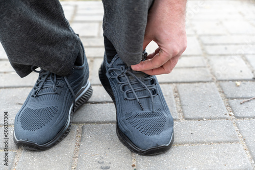 Bottom section of a mature man tying his shoelace. A man's hand tying a knot on the shoelace of his blue spore shoes. Outside. Daytime. Selective focus.