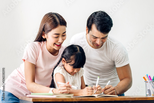 Portrait happy love asian family father and mother with little asian girl learn and study on table.Mom and dad with asian young girl writing with book make homework in homeschool at home.Education