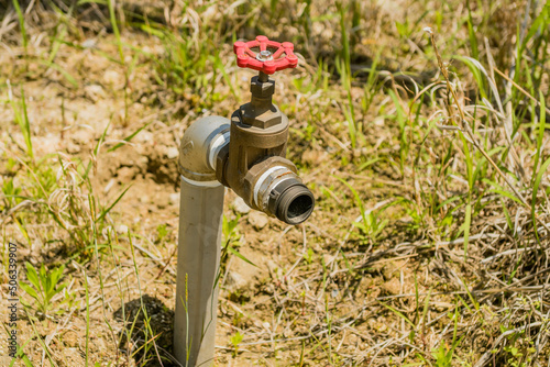 Metal water spigot with red tap in ground.