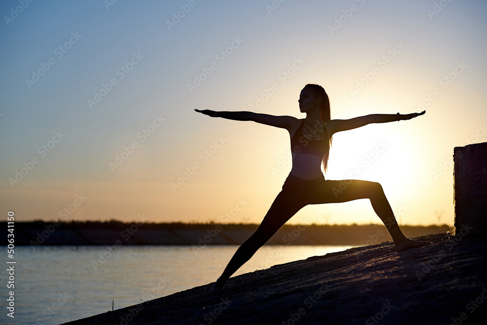 Silhouette woman practicing yoga or stretching on the beach pier at sunset or sunrise