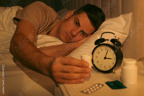 Man suffering from insomnia taking pill bottle in bed at night