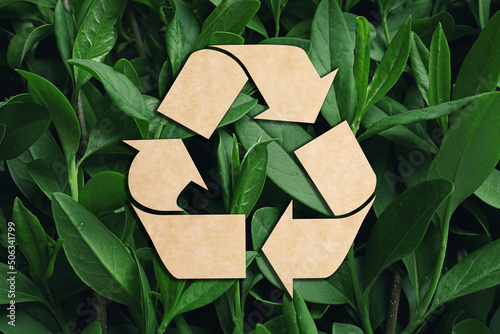 Recycling symbol cut out of kraft paper and fresh green leaves on background