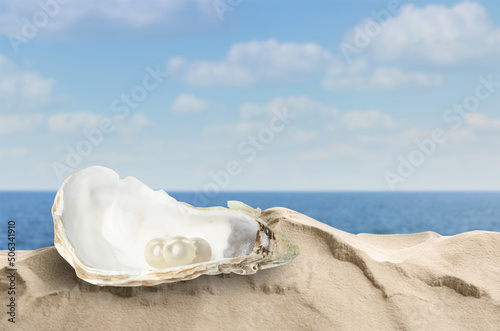 Open oyster shell with white pearls on sandy beach near sea