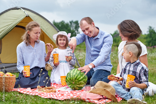 Happy family eating watermelon at picnic in meadow near the tent. Family Enjoying Camping Holiday In Countryside