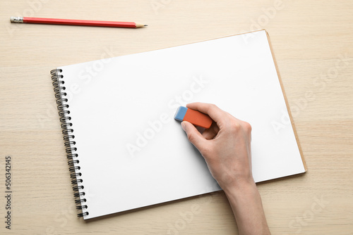 Woman erasing something in notebook at wooden table, closeup photo