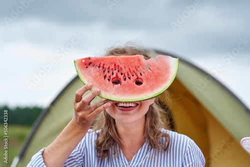 Funny woman eating watermelon on a picnic. Girl closed her eyes with a watermelon, looking into the holes