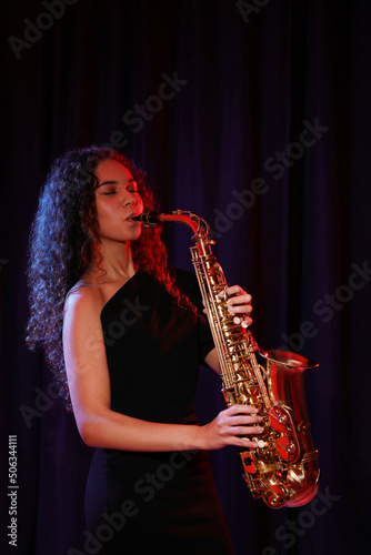 Beautiful African American woman playing saxophone on dark background