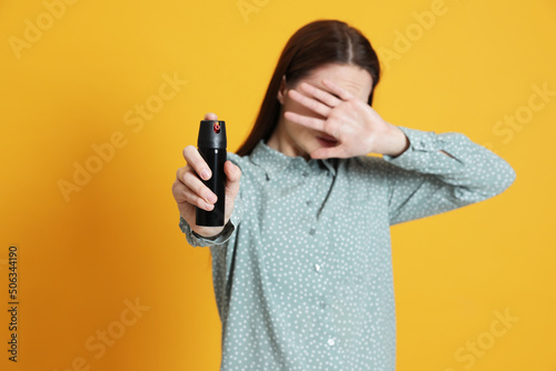 Photo Young woman covering eyes with hand and using pepper spray on yellow background
