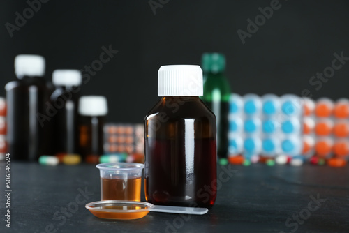 Bottle of cough syrup, dosing spoon and measuring cup on black table