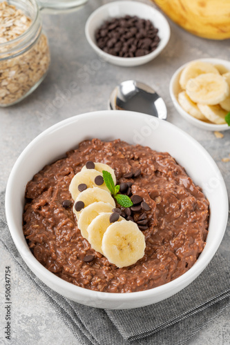 Chocolate oatmeal porridge with banana and chocolate chips on top in a white bowl. Healthy breakfast. Copy space.