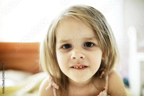 Little blonde girl lies on the bed. Emotional child infant posing.