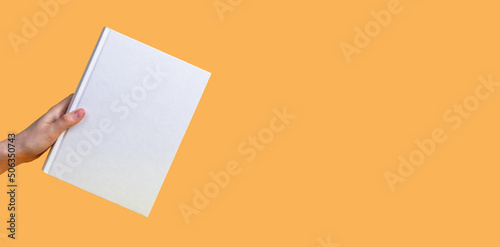 Banner with hand holding book mockup on orange background. Education, reading hobby, wisdom, intellectual development concept. Copy space. High quality photo