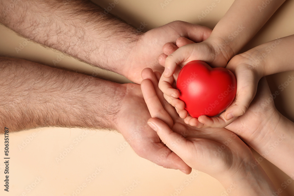 Parents and kid holding red heart in hands on beige background, top view Parents and kid holding red heart in hands on beige background, top view