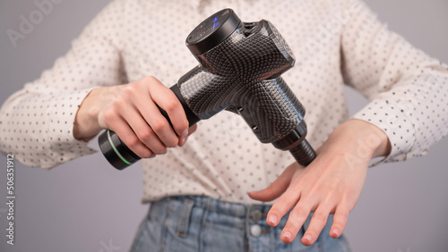 Caucasian business woman massaging her wrist with a percussion massager.