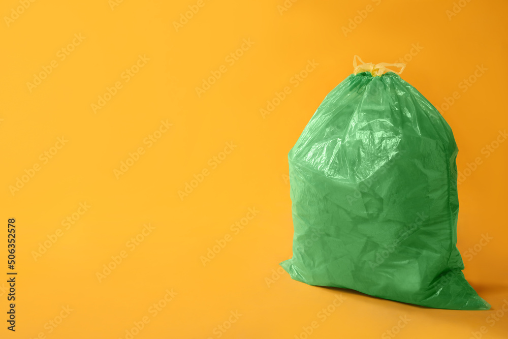 Trash bag full of garbage on yellow background. Space for text