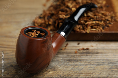 Fototapeta Naklejka Na Ścianę i Meble -  Smoking pipe with dry tobacco on wooden table, closeup