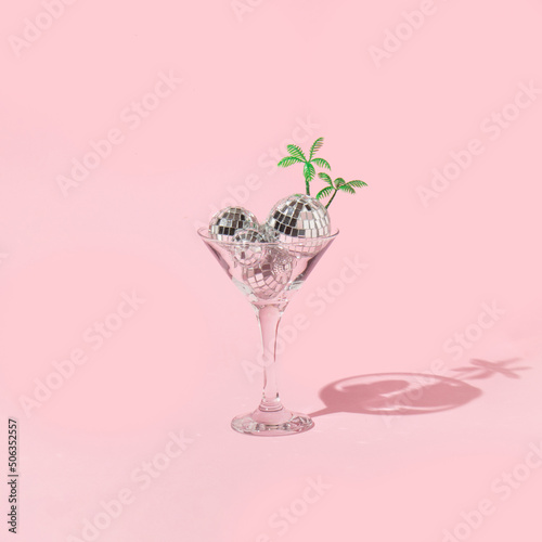 Summer tropical creative layout with martini cockatil glass with disco ball decoration and palm trees figurines on pastel pink background. 80s, 90s retro fashion aesthetic party concept. Pop art idea. photo