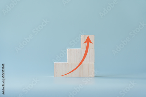 Red arrow going up on wooden blocks and light blue background. Concept of growing or improving.