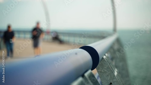 Close up of rail by water leading out to a pier as people walk in slow motion in the background. Slow motion. photo