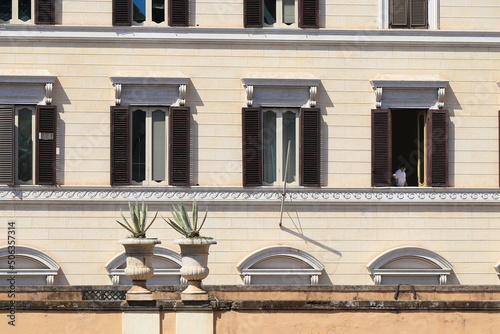 Building Facade Close Up with Windows, Brown Shutters and Two Agave Plants in Stone Pots on a Wall in Rome, Italy