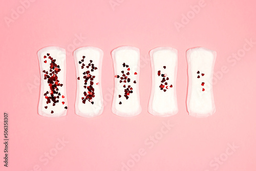 Sanitary napkins with different amount of hearts glitter of them on pink background.