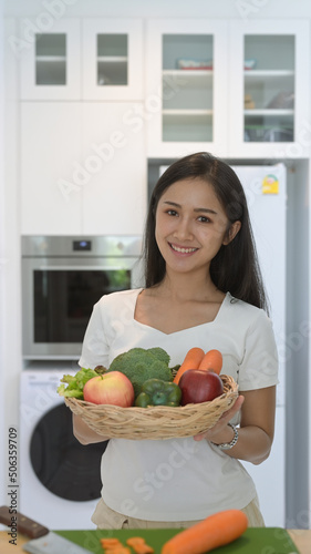 Portrait asian woman holding wicker basket with fresh organic vegetables and fruits standing in home office
